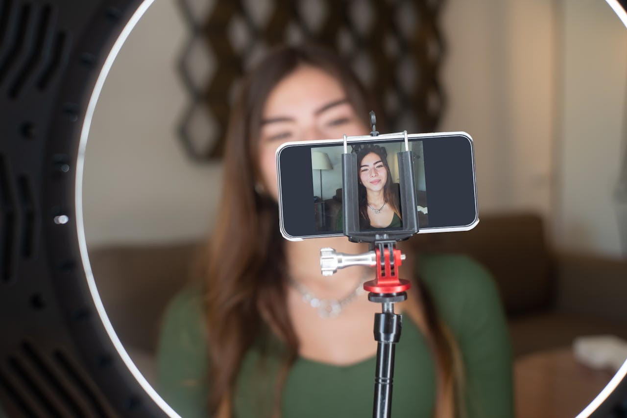 Services A young woman live streams from home using a smartphone and ring light setup.